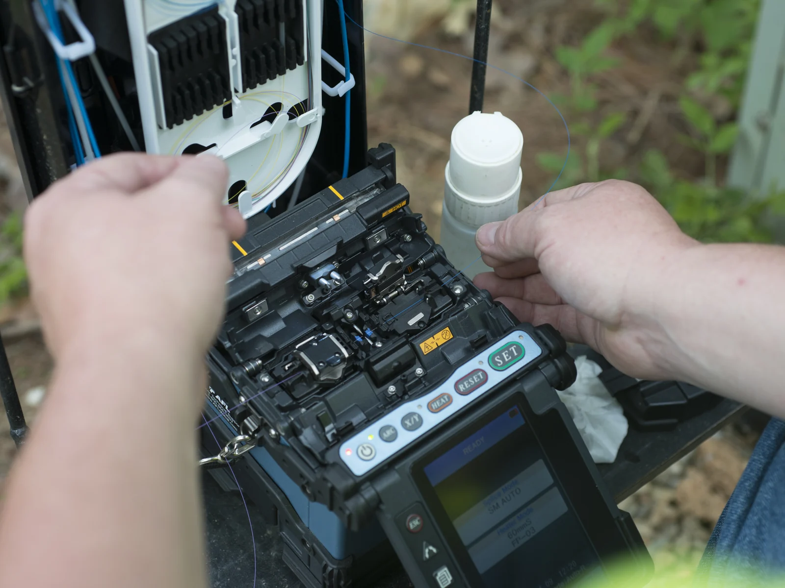 Hands working with fiber at a fusion splicer